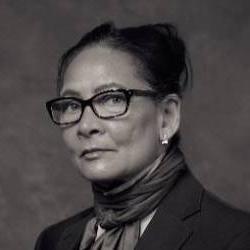 A black and white headshot of an artist wearing glasses with her hair pulled back